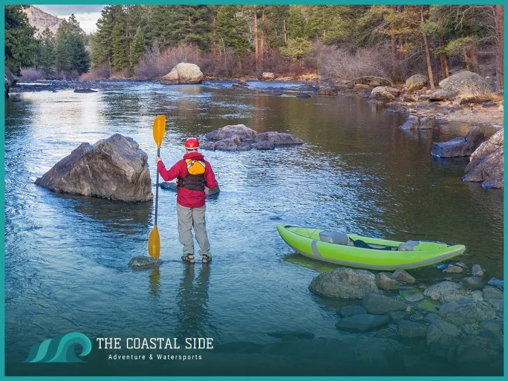 Man dressed for cold weather holding a kayak paddle standing near his kayak