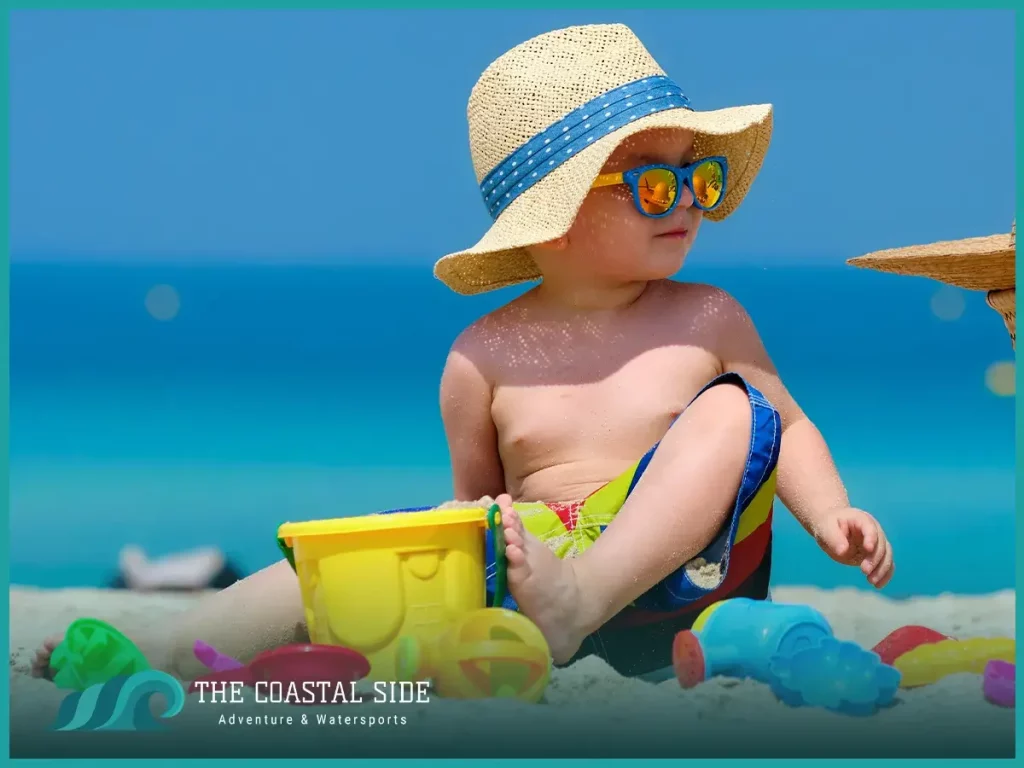 Little boy playing in the sand with a strap hat and beach toys