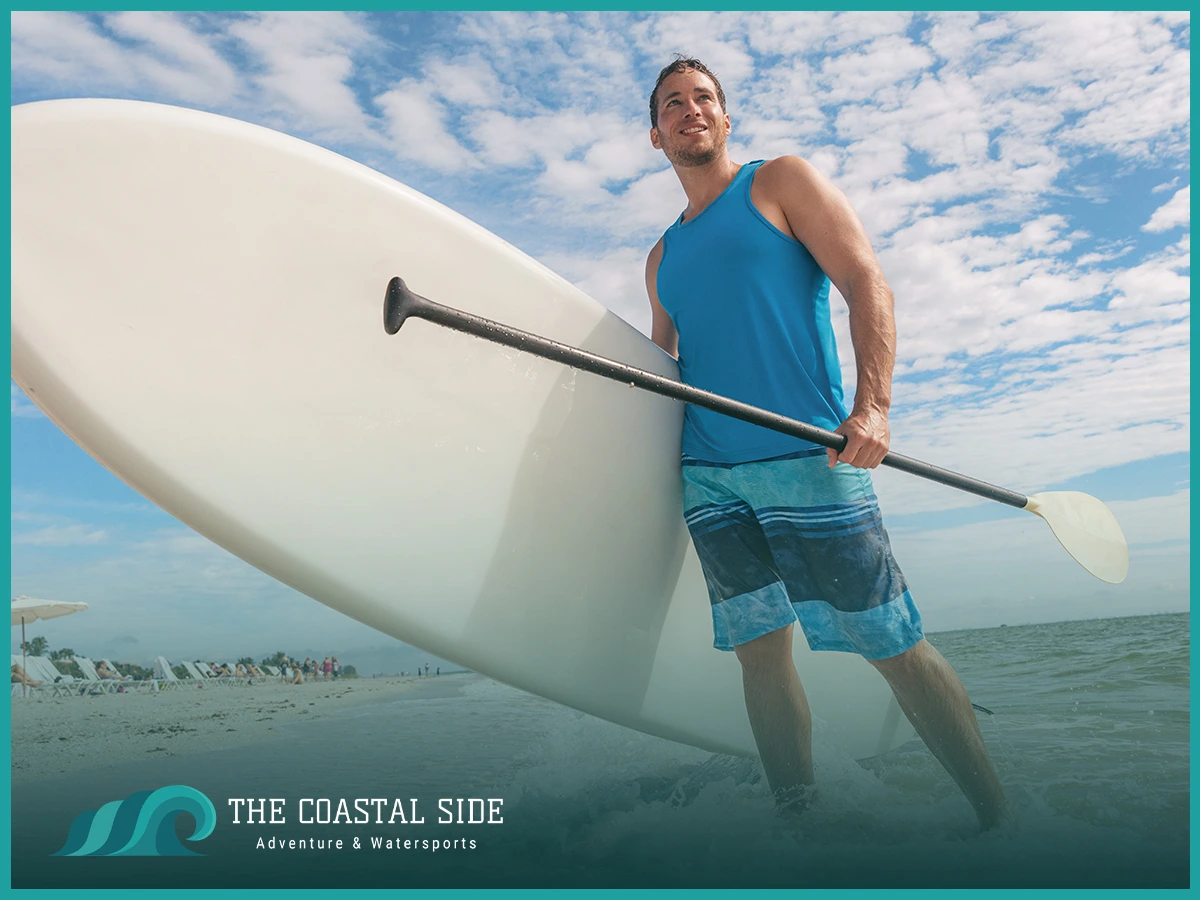 Man in blue swim trunks holding a stand up paddle board